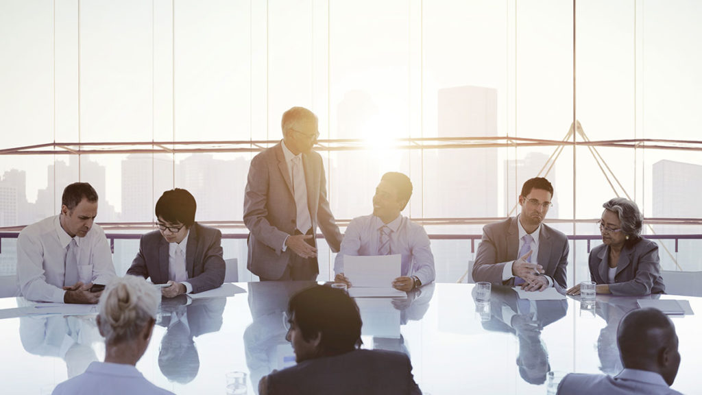 5 people sitting around a round table in an office environment reading paperwork