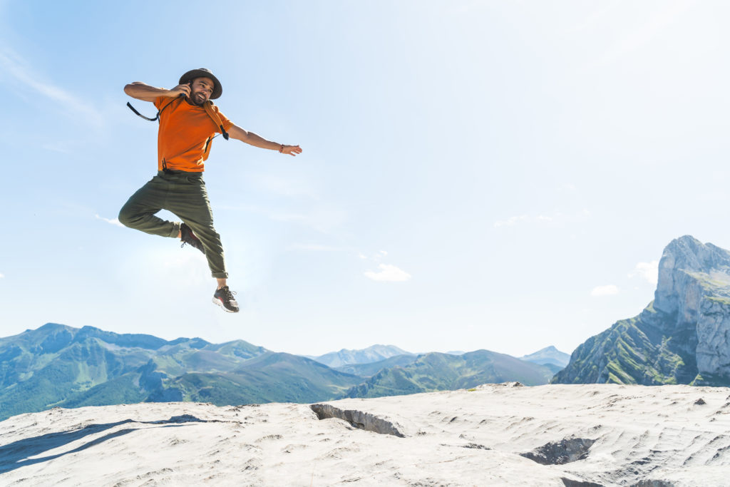 Happy man talking on a cellphone jumps in the air. There are mountains in the background.
